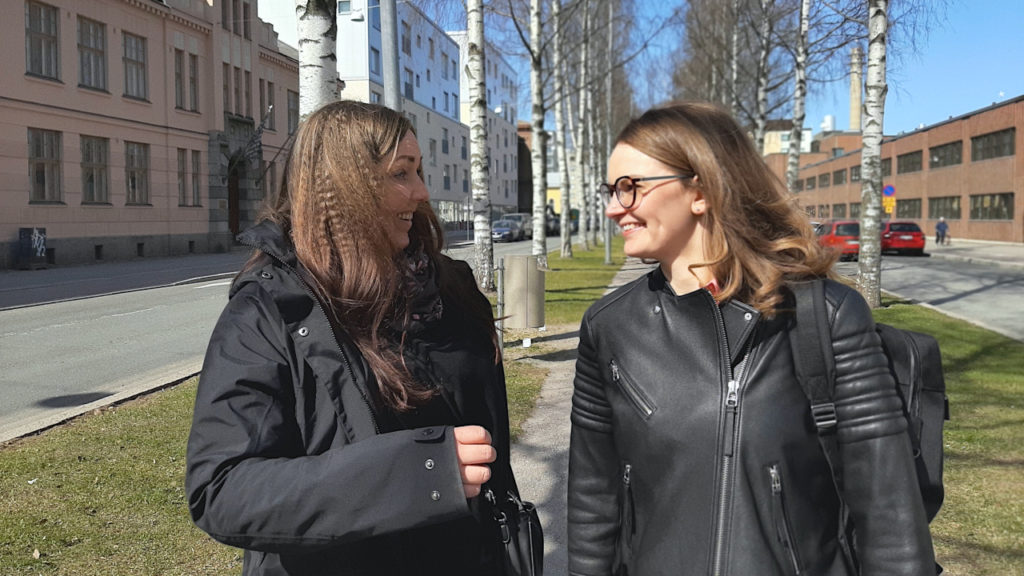 Johanna Leppänen ja Johanna Dahl katsovat iloisesti toisiaan, taustalla rakennuksia ja koivuja